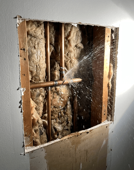 Burst copper pipe spraying water inside a wall cavity